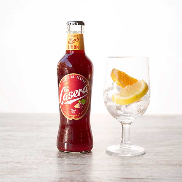 Botella de tinto de verano con limón y vaso con rodajas de naranja y limón