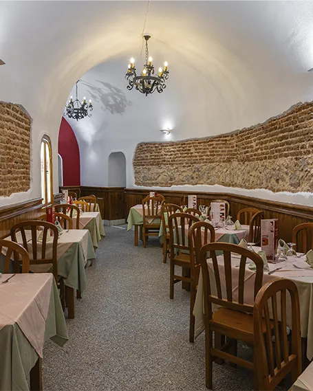 Salón interior en forma de cueva del Museo del Jamón en Plaza Mayor, Madrid, con mesas dispuestas para el servicio y paredes de ladrillo visto.