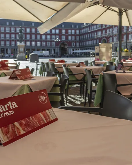 Terraza exterior del Museo del Jamón en Plaza Mayor, Madrid, con mesas preparadas bajo sombrillas y vista directa a la plaza.